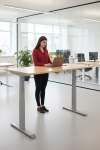 Frau an einem Steh-Sitz-Schreibtisch in einem Büro mit Laptop